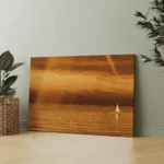 Lone sailboat on calm ocean water with golden reflections beneath an amber sunset sky